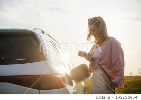 Young woman holding power supply cable from her electric car, prepared for charging it sustainable and economic transportation concept. 105258834