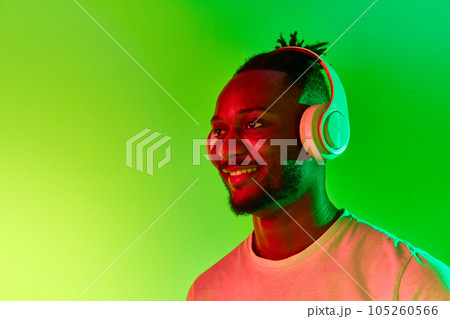 Image of young african man looking away in headphones and smiling over gradient colorful background in neon. Image of young african man looking away in headphones and smiling over gradient colorful background in neon. 105260566