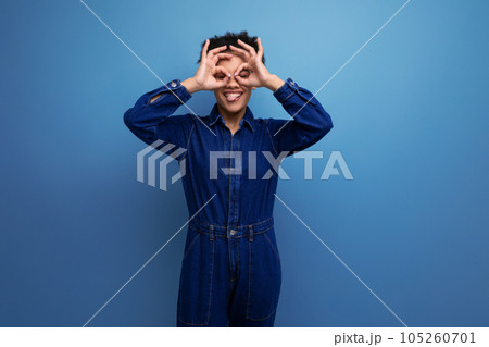 young cheerful positive brunette latin woman with afro hair gathered in a ponytail dressed in a blue young cheerful positive brunette latin woman with afro hair gathered in a ponytail dressed in a blue 105260701