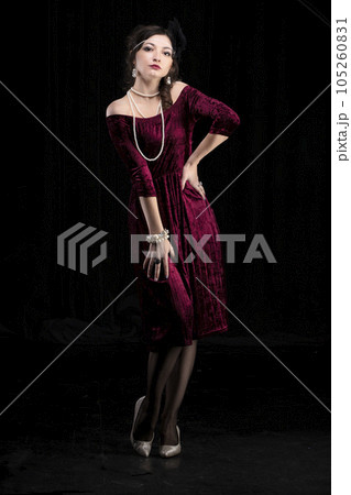 A beautiful girl dressed in the style of the 20-30s of the last century posing on a dark background. 105260831