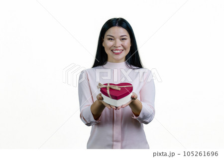 Young asian woman is giving you a heart-shaped gift box. Isolated on white background. Young asian woman is giving you a heart-shaped gift box. Isolated on white background. 105261696