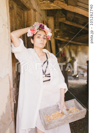 Beautiful indian woman in a white dress and a wreath on her head holds a basket with corn. The farm or countryside Beautiful indian woman in a white dress and a wreath on her head holds a basket with corn. The farm or countryside 105262740