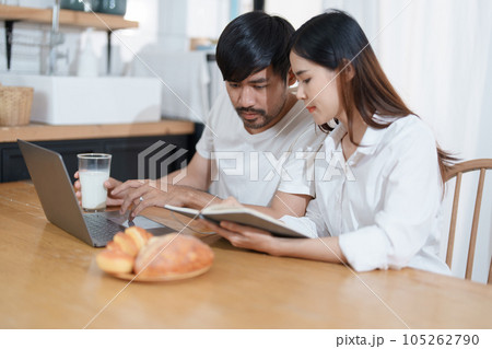 Young married couple showing happy smiling faces and using computers and notebooks to calculate household income and expenses while relaxing at home 105262790