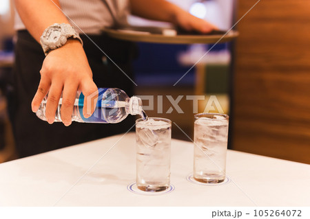 Waiter hand pouring water from bottel into a glass in restaurant. 105264072