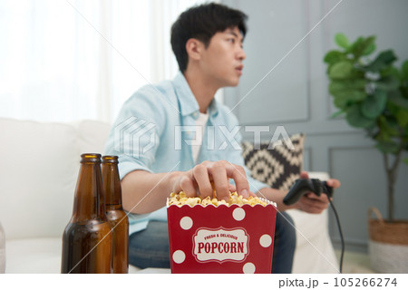 A young man sitting on a sofa, eating popcorn and watching TV 105266274