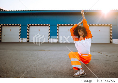 Young African American woman - dancer dancing in the street at sunset. Stylish woman with curly hair in an orange suit showing some moves Young African American woman - dancer dancing in the street at sunset. Stylish woman with curly hair in an orange suit showing some moves 105266753