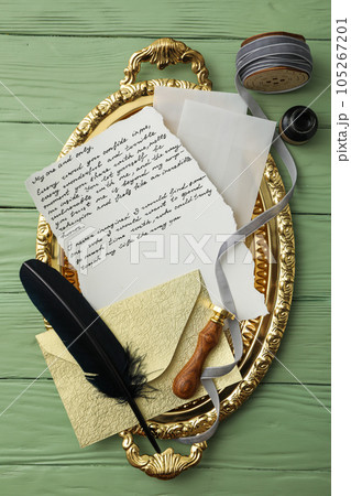 Golden tray with letter, feather and gray ribbon on green wooden background, top view 105267201