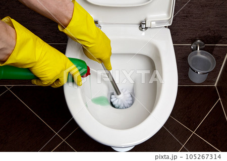 a person in yellow rubber gloves washes and disinfects toilet bowl with brush and disinfectant solution a person in yellow rubber gloves washes and disinfects toilet bowl with brush and disinfectant solution 105267314
