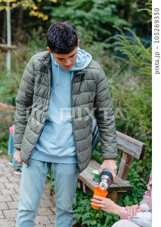 Happy Family drinking tea from a thermos in the forest. Photo of cute charming mother with childrens dressed casual outfit walking sitting bench drinking tea smiling outside city park 105269350