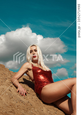 Beautiful blond woman in a red sexy dress on the background of the sky and sand. Beautiful blond woman in a red sexy dress on the background of the sky and sand. 105271498