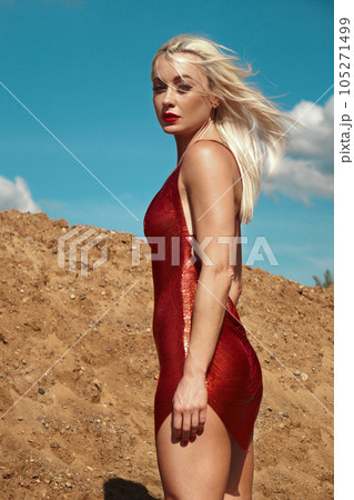Beautiful blond woman in a red sexy dress on the background of the sky and sand. 105271499