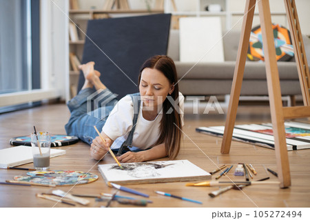 Brunette lying on floor and painting picture in living room Brunette lying on floor and painting picture in living room 105272494