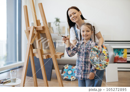 Mom with child's hand and brush standing near easel at home 105272895