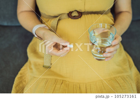 Prenatal Vitamins. Portrait Of Beautiful Smiling Pregnant Woman Holding Supplement and a glass of water, Taking Supplements For Healthy Pregnancy While Sitting On Couch At Home, Free Space Prenatal Vitamins. Portrait Of Beautiful Smiling Pregnant Woman Holding Supplement and a glass of water, Taking Supplements For Healthy Pregnancy While Sitting On Couch At Home, Free Space 105273161