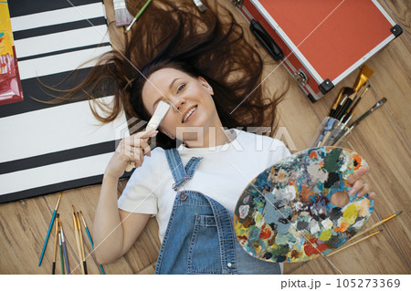Woman with palette covering one eye with brush on floor Woman with palette covering one eye with brush on floor 105273369