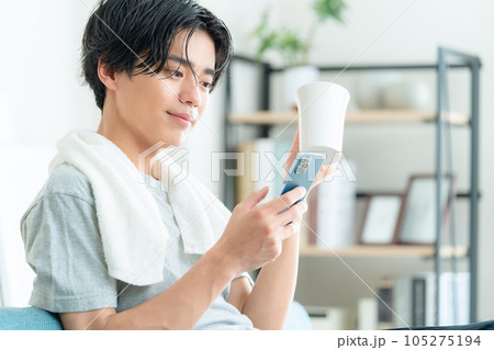 リビングで風呂上がりにコーヒーを飲みながらスマホを操作する若い男性 105275194