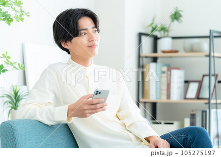 リビングでソファに座ってスマホを操作する若い男性 105275197