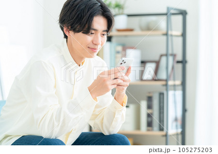 リビングでソファに座ってスマホを操作する若い男性 リビングでソファに座ってスマホを操作する若い男性 105275203