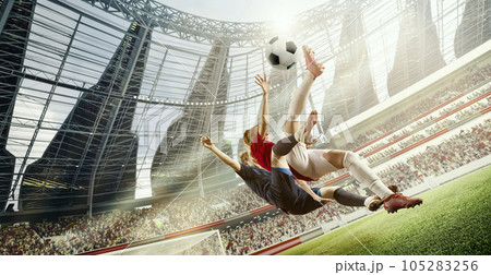 Tense game moment. Dynamic image of two women, football players in motion, hitting ball in jump during match on 3D open air stadium Tense game moment. Dynamic image of two women, football players in motion, hitting ball in jump during match on 3D open air stadium 105283256
