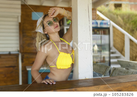 Sexy girl in sunglasses and swimsuits posing near beach bar Sexy girl in sunglasses and swimsuits posing near beach bar 105283826