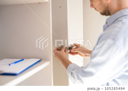 A man screws a furniture loop to the cabinet door A man screws a furniture loop to the cabinet door 105285494