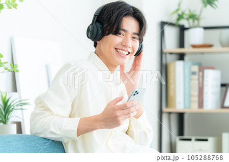 リビングでソファに座ってスマホとヘッドホンで音楽を聴く若い男性 リビングでソファに座ってスマホとヘッドホンで音楽を聴く若い男性 105288768