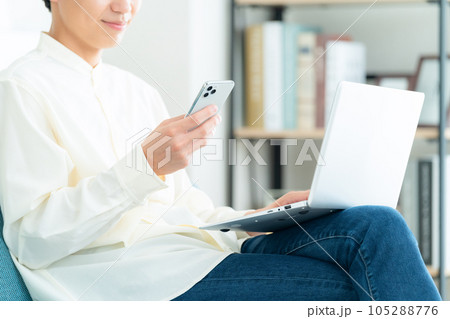 リビングでソファに座ってパソコンを操作する若い男性のボディパーツ 105288776