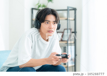 リビングでソファに座ってヘッドホンをつけてゲームをする若い男性 105288777
