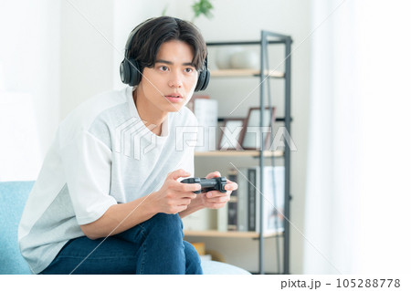 リビングでソファに座ってヘッドホンをつけてゲームをする若い男性 リビングでソファに座ってヘッドホンをつけてゲームをする若い男性 105288778
