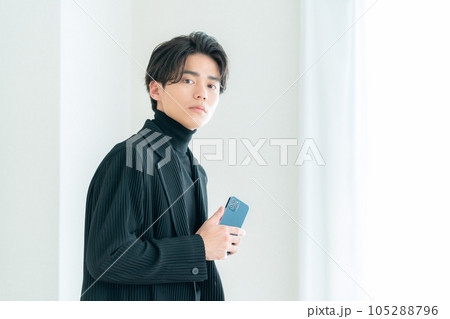 リビングの窓際でスマホを操作する若い男性 リビングの窓際でスマホを操作する若い男性 105288796