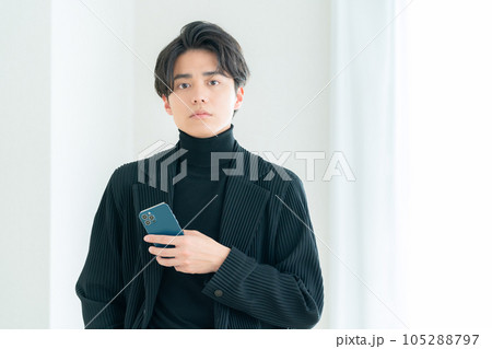 リビングの窓際でスマホを操作する若い男性 105288797