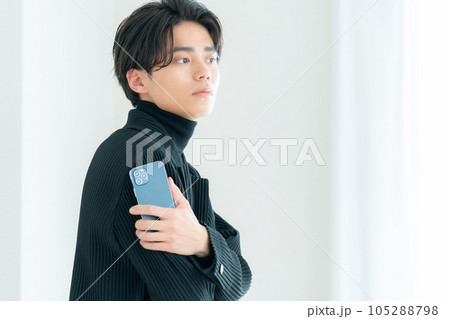 リビングの窓際でスマホを操作する若い男性 リビングの窓際でスマホを操作する若い男性 105288798