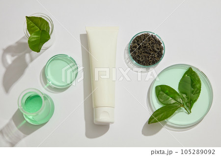 Concept for advertising and branding cosmetic with ingredient from green tea. Blank plastic cosmetics container for cream or cleanser displayed with green tea leaves and glassware on white background Concept for advertising and branding cosmetic with ingredient from green tea. Blank plastic cosmetics container for cream or cleanser displayed with green tea leaves and glassware on white background 105289092