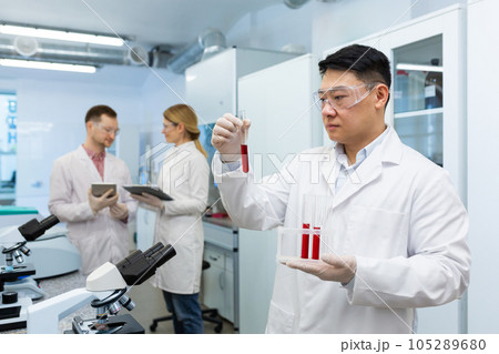 Serious asian scientist inside laboratory researching blood in test tubes, man in medical white coat. Serious asian scientist inside laboratory researching blood in test tubes, man in medical white coat. 105289680