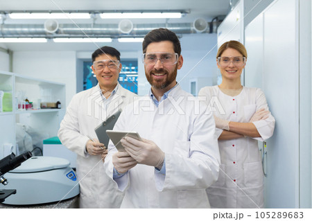 Successful team of scientists, three persons man and woman smiling and looking at the camera, portrait of a group of scientists in white medical coats inside a laboratory. 105289683