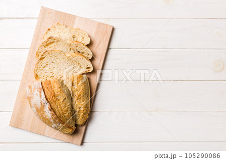 Freshly baked bread slices on cutting board against white wooden background. top view Sliced bread 105290086