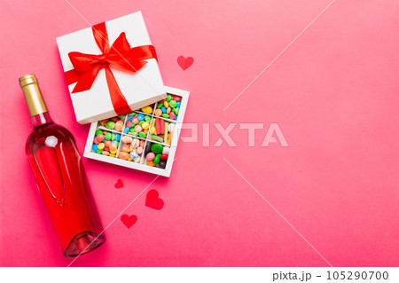 Bottle of red wine on colored background for Valentine Day with gift and chocolate. Heart shaped with gift box of chocolates top view with copy space Bottle of red wine on colored background for Valentine Day with gift and chocolate. Heart shaped with gift box of chocolates top view with copy space 105290700
