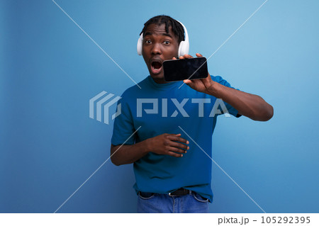 african guy in a t-shirt listens to music using headphones and smartphone african guy in a t-shirt listens to music using headphones and smartphone 105292395