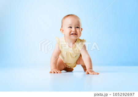 Cute, lovely, funny baby girl, child, toddler smiling and crawling on floor against blue studio background Cute, lovely, funny baby girl, child, toddler smiling and crawling on floor against blue studio background 105292697