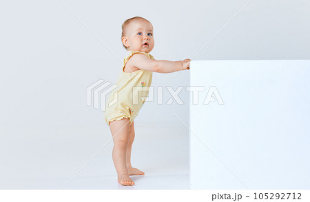 Adorable little baby girl, child, toddler in comfortable cute clothes standing and looking against grey studio background Adorable little baby girl, child, toddler in comfortable cute clothes standing and looking against grey studio background 105292712
