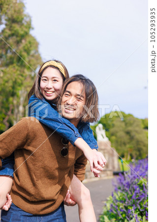 花畑の前でおんぶする彼氏と彼女 105293935