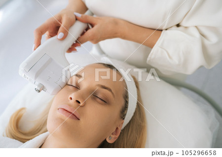 Close-up face of young woman receiving HUFU therapy high intensity ultrasound treatment on face. Cosmetologist doing non-surgical cosmetic plasma lift on female client with ultrasonic device. 105296658