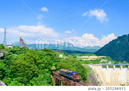 阿蘇山を背景に鉄橋を横断するトロッコ列車風景「全線開通・運航再開」(立野駅・立野ダム周辺から撮影) 105296931