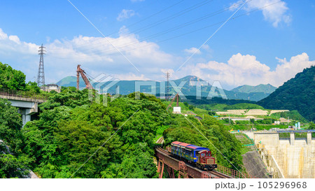 阿蘇山を背景に鉄橋を横断するトロッコ列車風景「全線開通・運航再開」(立野駅・立野ダム周辺から撮影) 105296968