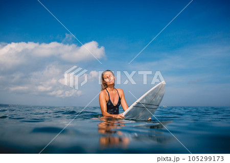 Surfer woman sitting on surfboard and wait waves. Woman with surfboard in ocean Surfer woman sitting on surfboard and wait waves. Woman with surfboard in ocean 105299173