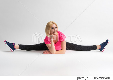 A woman in sportswear and sneakers sits in a transverse split 105299580