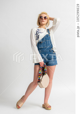 Woman in rustic casual summer clothes with a handbag straightens her hair with her hand 105299819