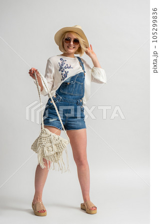 Happy woman in rustic casual clothes, wearing a hat and sunglasses and holding a handbag 105299836