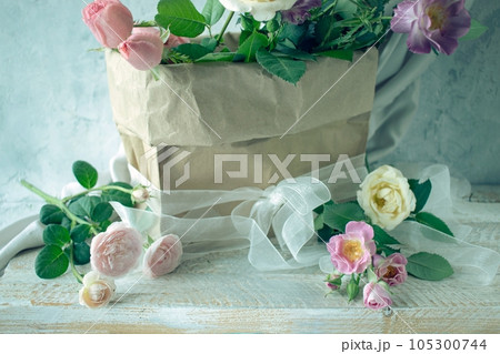 Bouquet of fresh roses in pastel shades, in craft paper packaging, against a gray concrete wall and silk fabric, still life Bouquet of fresh roses in pastel shades, in craft paper packaging, against a gray concrete wall and silk fabric, still life 105300744