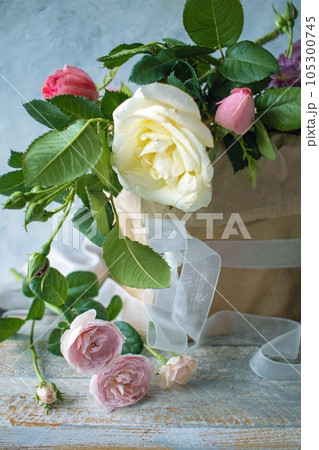 Bouquet of fresh roses in pastel shades, in craft paper packaging, against a gray concrete wall and silk fabric, still life  105300745